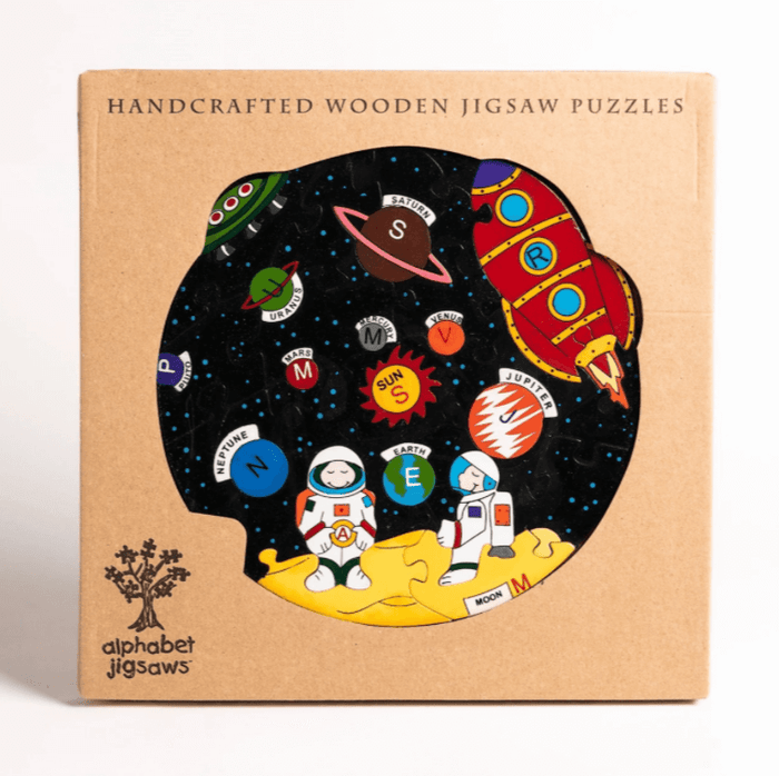 Space-themed wooden puzzle in a brown box with a window showing colorful planets, a red rocket, and astronauts.