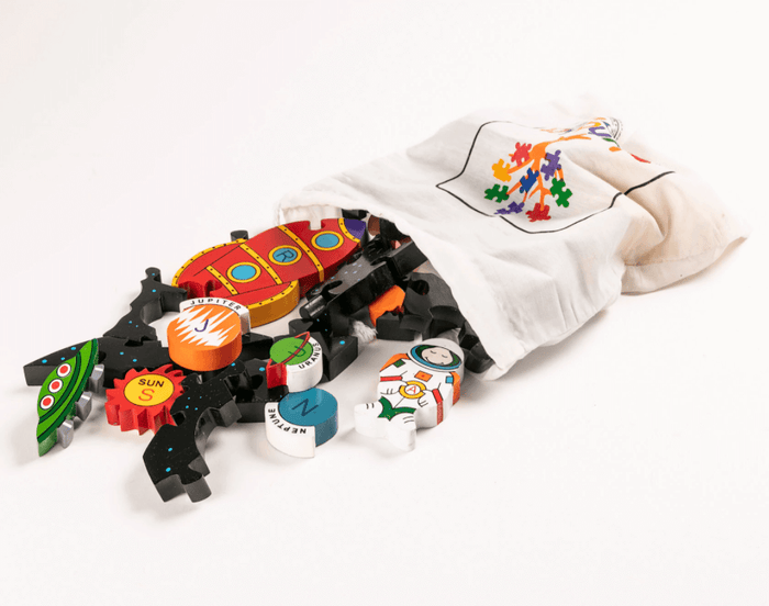 Colorful wooden rocket, planet, and astronaut puzzle pieces spilling out of a white fabric drawstring bag.