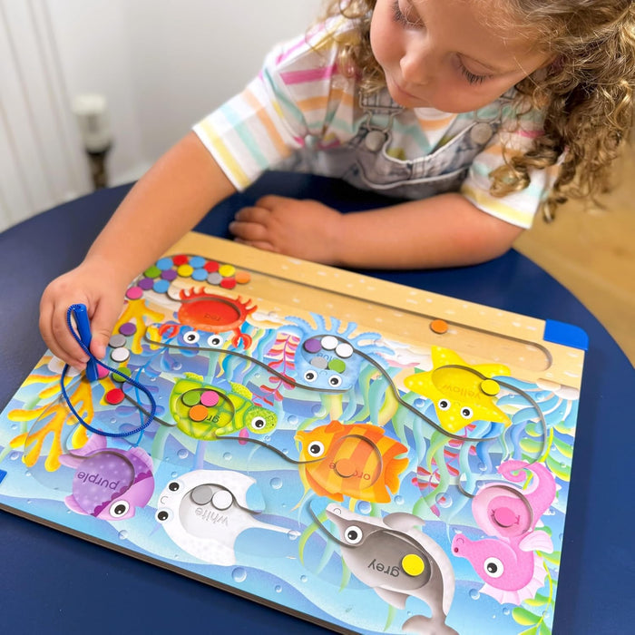 Toddler sorts colored discs with a magnetic wand into matching sea animal slots on a vibrant wooden puzzle board.