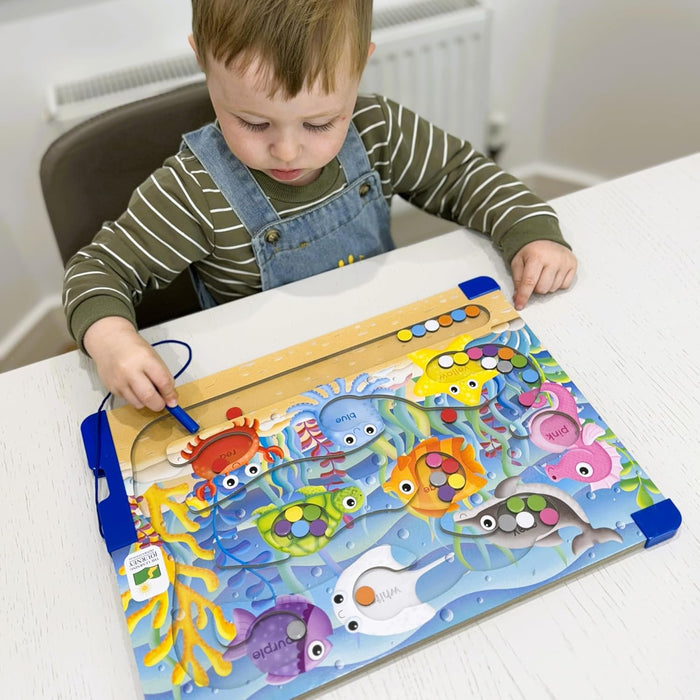 Toddler using a magnetic wand to sort colorful beads into matching sea creatures on an underwater wooden puzzle board.