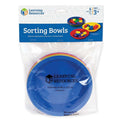 Six rainbow-colored, round plastic bowls stacked inside a clear retail bag with a brand header.