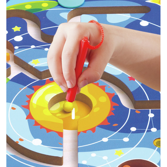 Close-up of a hand using a red magnetic wand to move a yellow bead through a space-themed wooden maze puzzle.