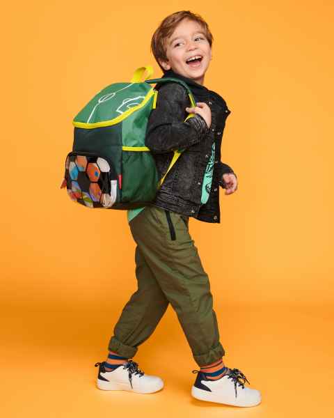 Green and yellow soccer backpack with a ball pattern pocket worn by a child against a bright orange background.