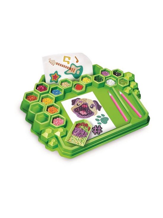 Green craft tray with hexagonal gem compartments, colorful rhinestones, pink tools, and dog and guitar templates.