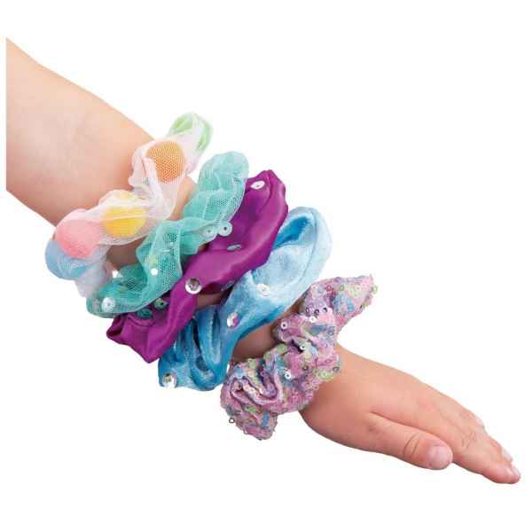 Child’s arm wearing five colorful scrunchies featuring pom-poms, sequins, and rhinestones.