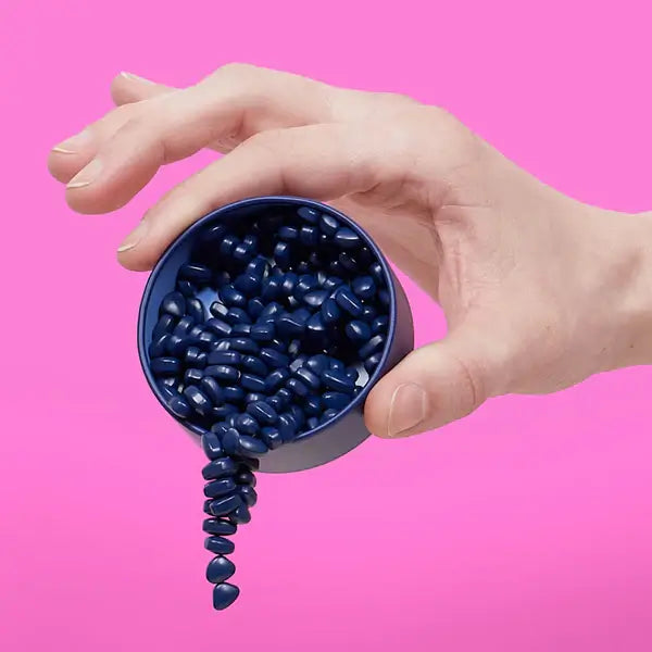 Hand holding a navy tin of dark blue magnetic stones against pink, with stones spilling out in a linked chain.
