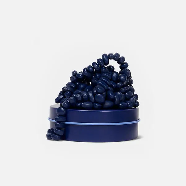Irregular navy blue magnetic pebbles clustered on a matching round navy blue tin with a light blue rim.
