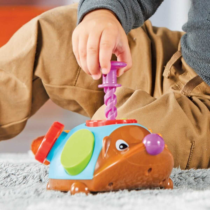 Child pushes a purple spiral plunger into a brown hedgehog toy with a blue back and colorful fidget buttons.