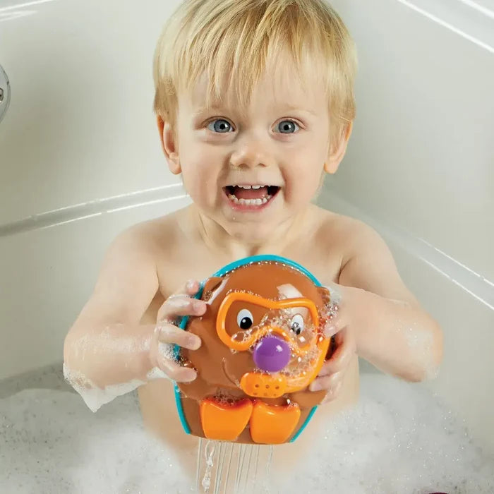 Toddler in a bubble bath holding a brown hedgehog toy with orange goggles, a purple nose, and orange flippers.