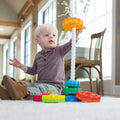 Toddler stacking colorful gear-shaped discs onto a white spiral pole toy while sitting on a white rug.