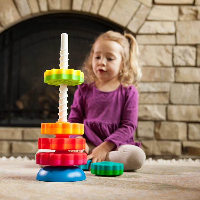 Toddler girl plays with colorful gear-shaped discs spinning down a white spiral rod on a blue base.