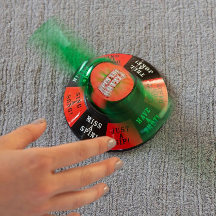 Hand near a spinning green bottle on a circular base with segments labeled Have a Shot, Truth or Dare, and Tell a Joke.