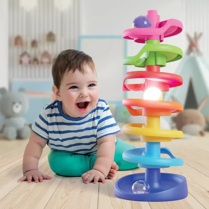 Smiling baby next to a colorful seven-tier spiral ball tower toy with a glowing light-up ball.