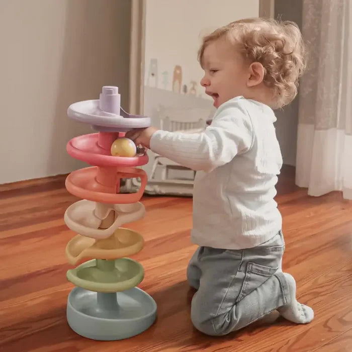 Toddler plays with a 7-tier spiral ball drop tower featuring muted pastel ramps on a wooden floor.