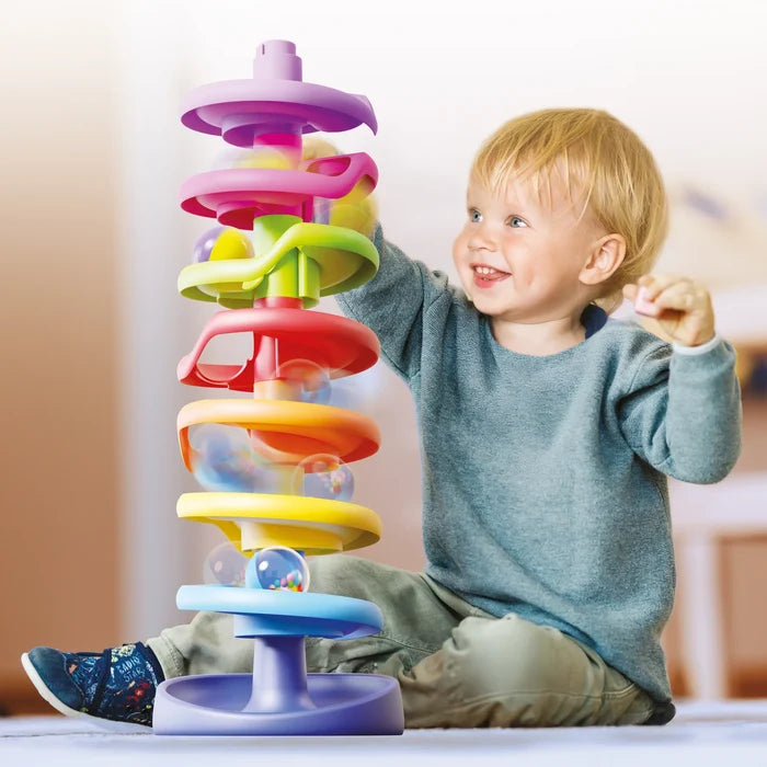 Toddler playing with a seven-tier rainbow spiral ramp tower as clear balls roll down the colorful tracks.