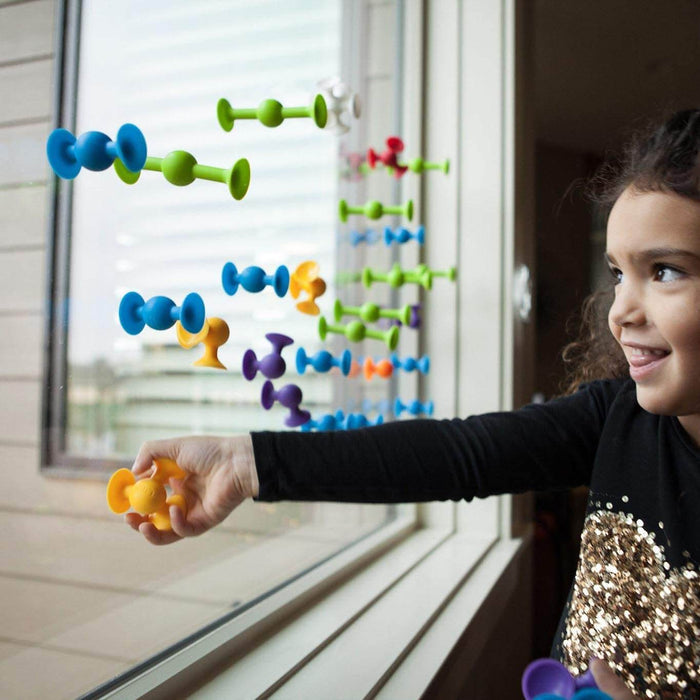 A child sticks colorful, flexible suction cup toys in blue, green, and orange onto a glass window while smiling.