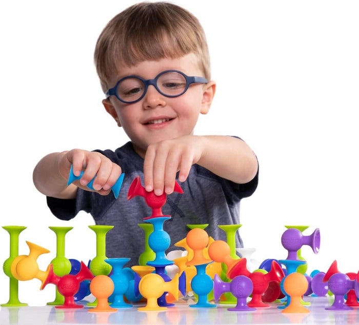 Young boy with glasses playing with colorful, silicone suction cup building toys in various shapes and sizes.