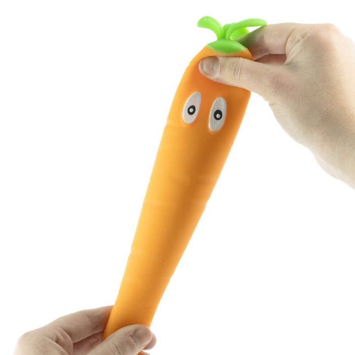 A long, bright orange squishy carrot toy with cartoon eyes and green leaves being pulled by hands.