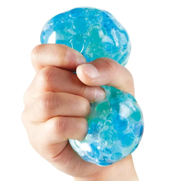 Hand squeezing a translucent squishy ball filled with small blue and teal water beads.