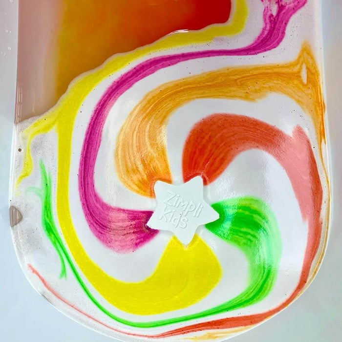 White star-shaped bath bomb dissolving in water, creating vibrant swirls of pink, orange, yellow, and green.