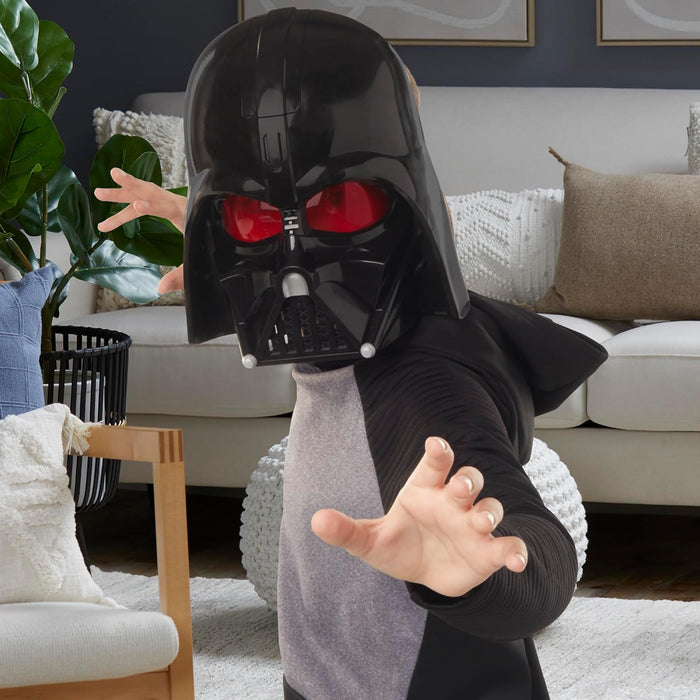 Child wears a black Darth Vader electronic mask with glowing red eyes and reaches toward the camera.