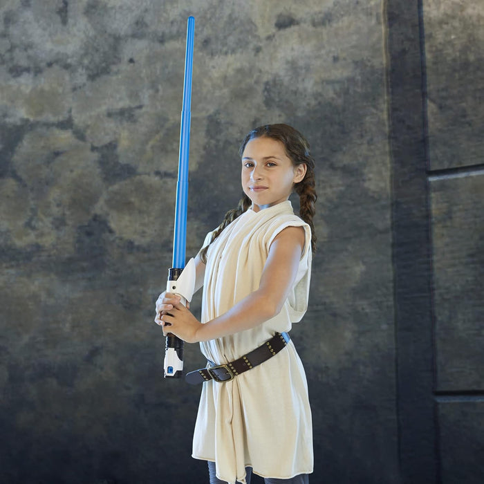 Child holding a toy lightsaber with a blue blade and white and black hilt, wearing a beige Jedi-style tunic.