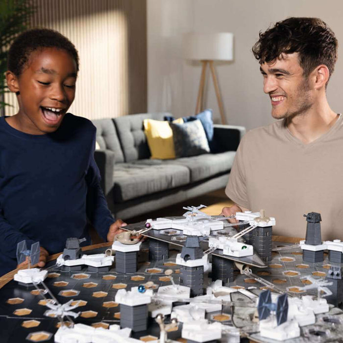 Boy and man play with a Star Wars marble run featuring a hexagonal grid, gray towers, and TIE fighter models.