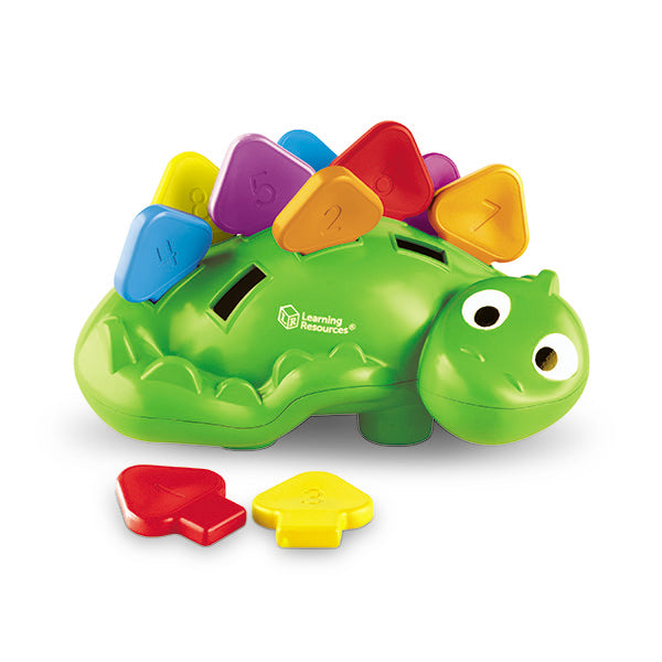Green toy dinosaur with colorful numbered scales on its back and two loose scales sitting in front.