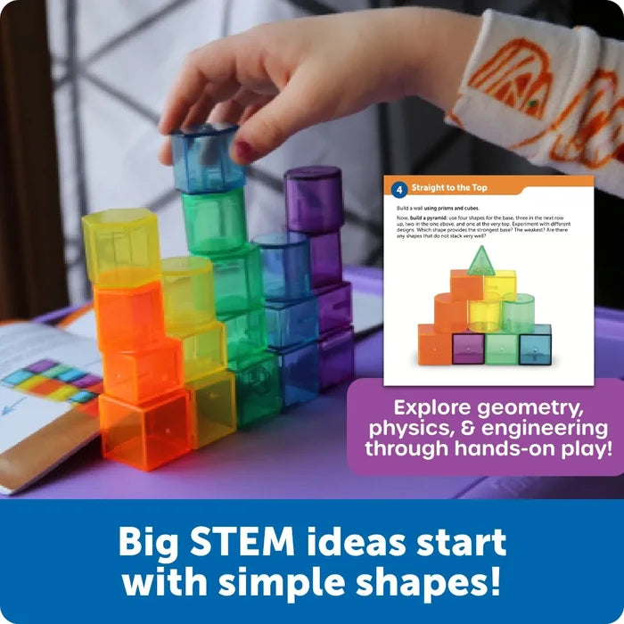 Child stacks colorful translucent 3D shapes like cubes and cylinders into towers with a STEM challenge card.