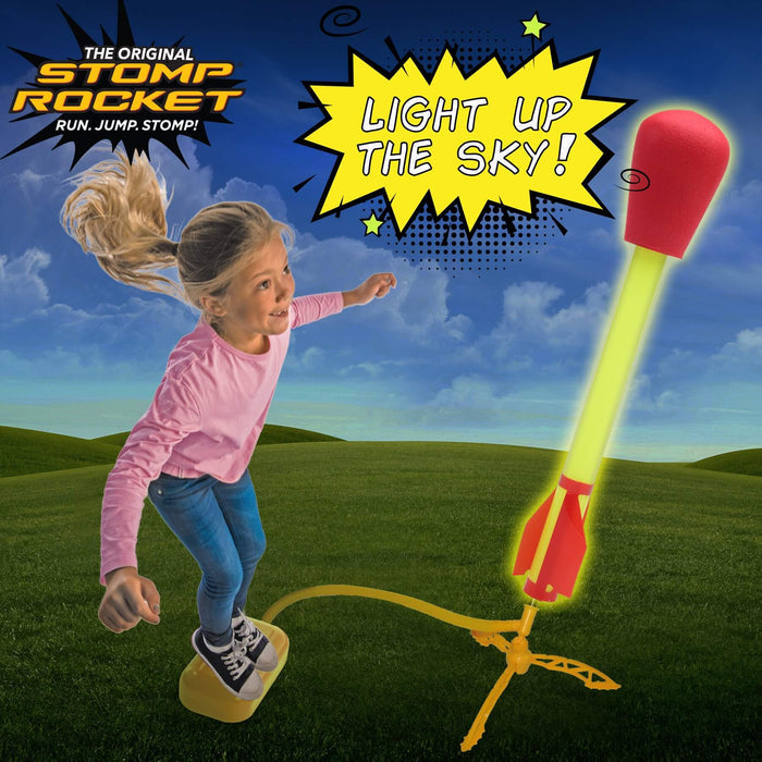 A girl jumps on a yellow pad launching a glowing LED rocket with a red foam tip and red fins into a blue sky.
