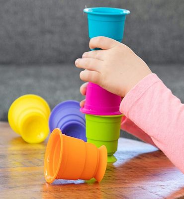 A child's hand stacks colorful silicone suction cups in blue, pink, and green on a wooden table.