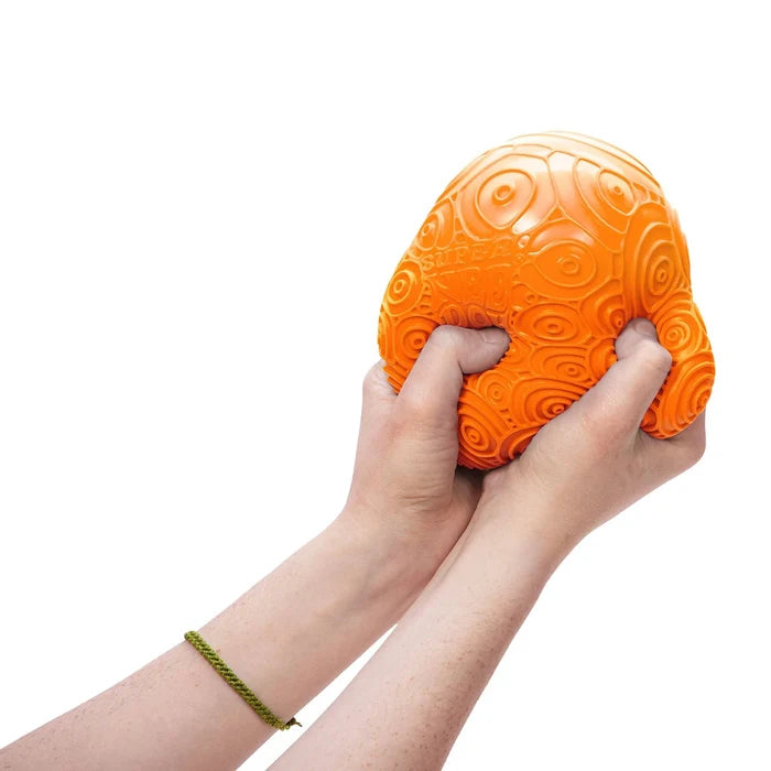 Two hands squeezing a large, bright orange squishy ball with a textured pattern of concentric circles and ripples.