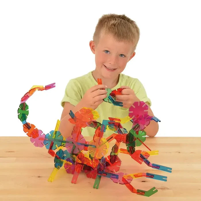 Young boy building a colorful dragon with translucent octagonal and rectangular interlocking plastic pieces.