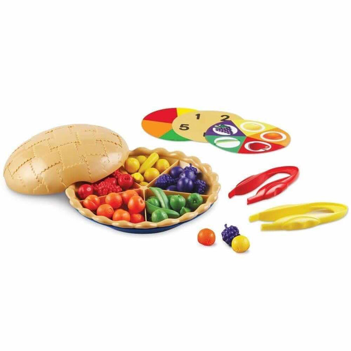 Plastic toy pie with colorful fruit, sorting cards, and red and yellow jumbo tweezers on a white background.