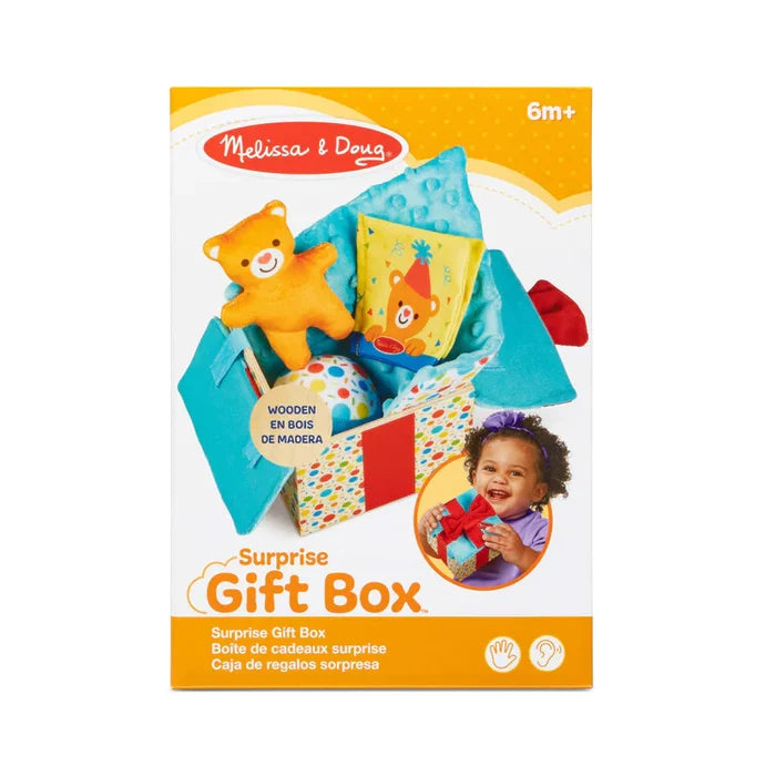 Packaging for a baby toy with a plush orange bear and ball inside a colorful, open polka-dot fabric gift box.