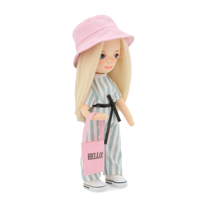 Blonde doll in a pink bucket hat and green striped jumpsuit holding a pink tote bag with HELLO! text.
