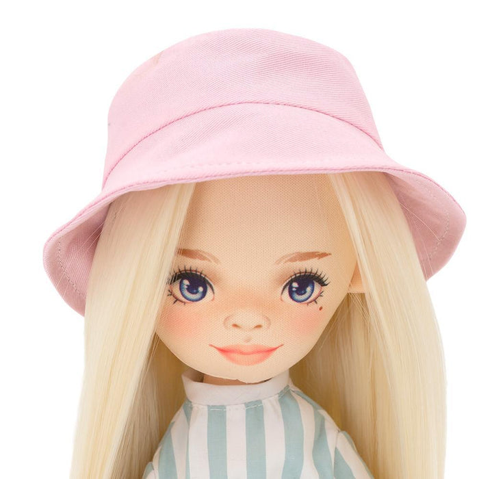 Blonde doll with blue eyes wearing a pink bucket hat and a light blue and white striped jumpsuit.