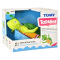 Lime green plastic bath turtle toy in a white cardboard box with Toomies branding, wearing a colorful striped swimsuit.