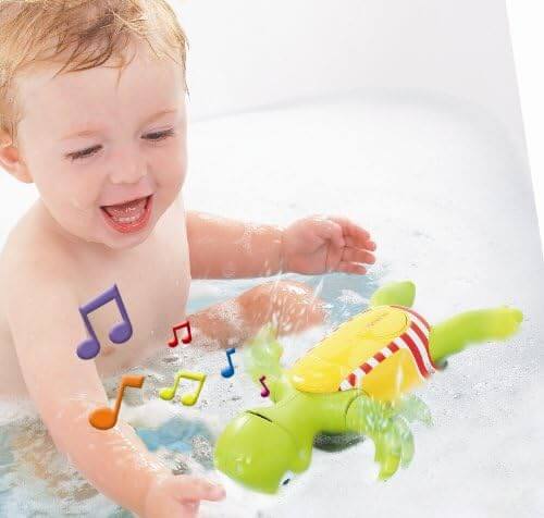 Smiling baby in a bathtub playing with a green toy turtle featuring colorful musical note graphics.