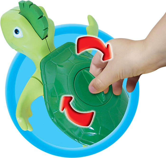Hand winding a green toy turtle by turning the circular dial on its shell, shown with red rotation arrows.