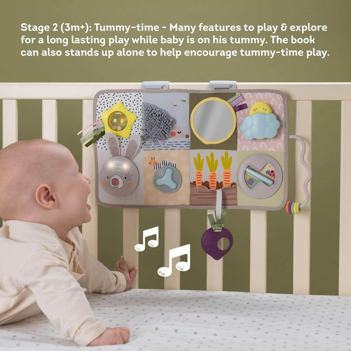 Baby on tummy in a crib looking at a colorful sensory board with a mirror, rabbit, and garden-themed toys.