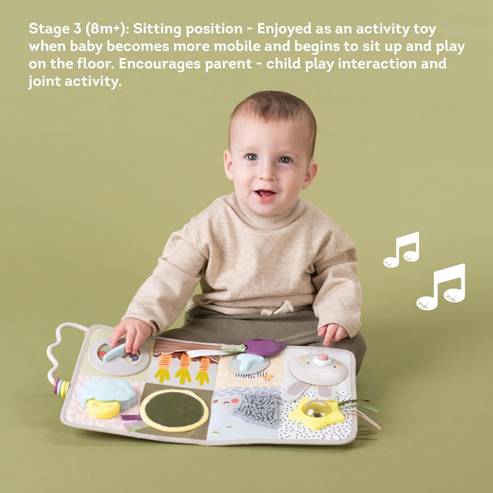 A baby sits playing with a colorful fabric activity board featuring garden-themed textures, a mirror, and shapes.