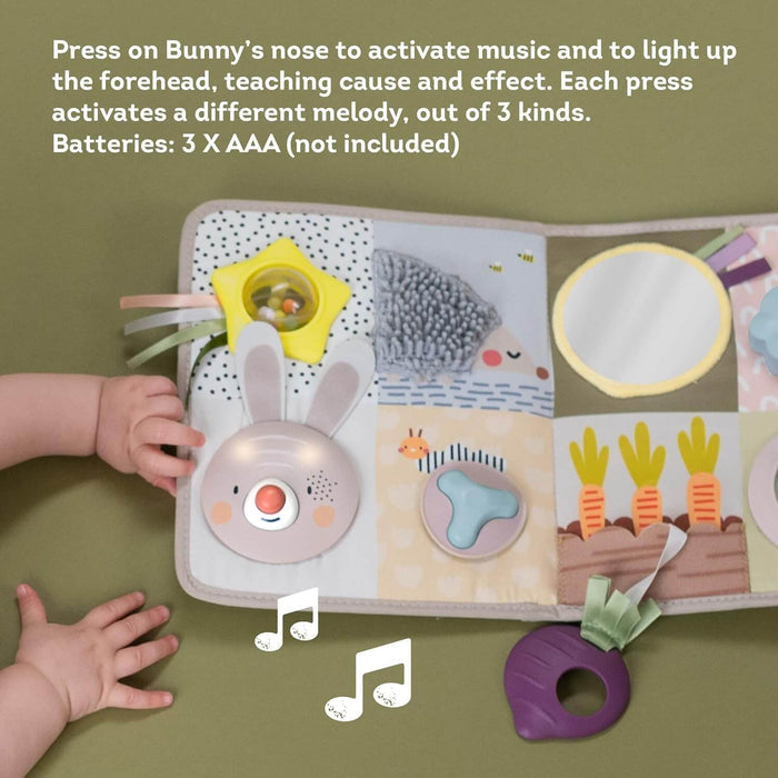 Baby reaching for a soft activity center featuring a light-up bunny, star rattle, mirror, and garden illustrations.