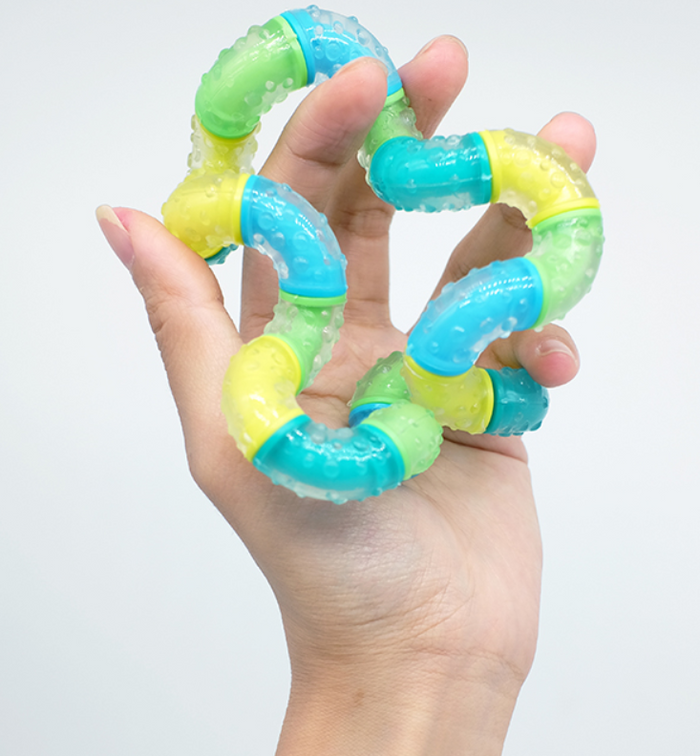 Hand holding a bumpy, translucent fidget toy with interlocking blue, green, and yellow curved segments.