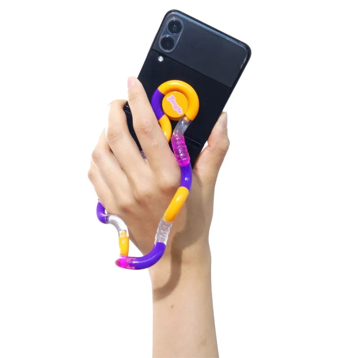 Hand holding a black smartphone with a purple, orange, and clear twisty Tangle fidget toy attached to the back.