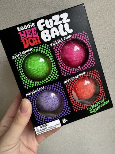 Hand holding a black box with four round windows showing neon green, pink, purple, and orange fuzzy balls.