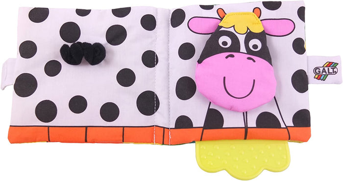 Open cow-print soft book with a plush pink cow face, black fuzzy tail, and a yellow scalloped teether at the bottom.
