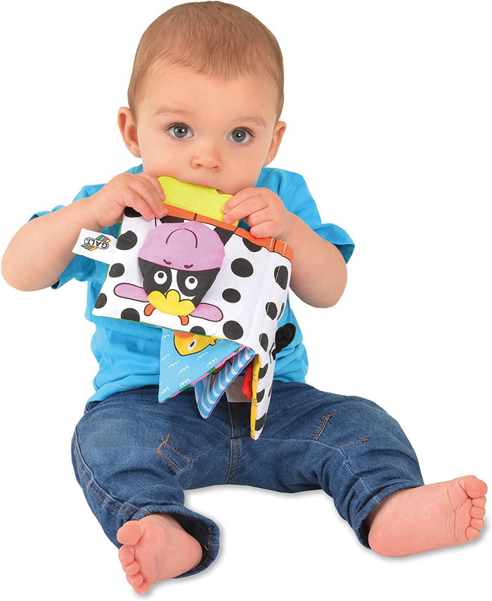 Baby chewing a soft book with black and white cow spots, a pink cow face, and a yellow textured teether edge.