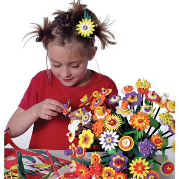 Young girl building a large bouquet of layered foam flowers in vibrant shades of yellow, purple, and orange.