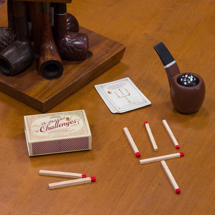Sherlock Holmes matchstick puzzle with wooden pipe, challenge box, cards, and red-tipped matches on a wooden table.